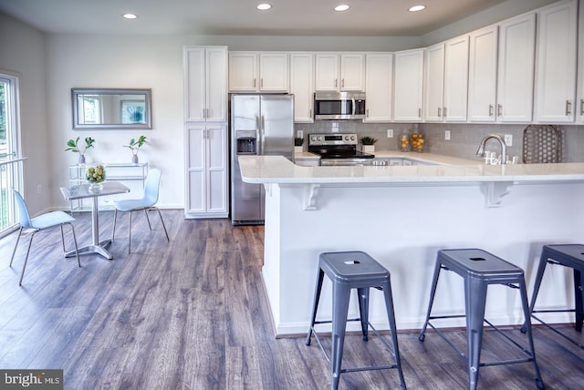 kitchen featuring white cabinetry, stainless steel appliances, tasteful backsplash, dark hardwood / wood-style flooring, and a breakfast bar