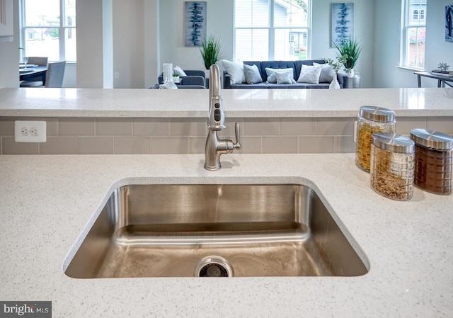 details with backsplash, light stone counters, and sink