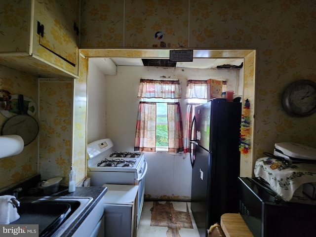 kitchen featuring black fridge, white gas range, and sink