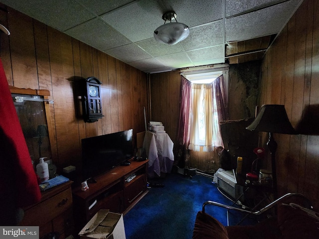 misc room featuring dark colored carpet, a paneled ceiling, and wood walls