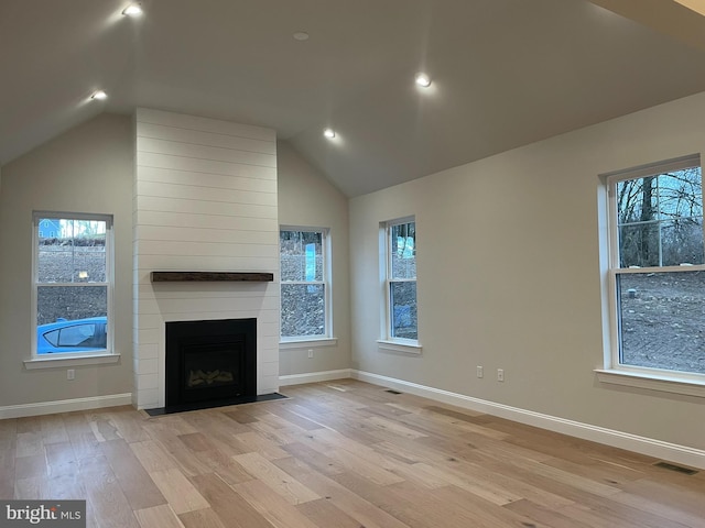 unfurnished living room with a large fireplace, plenty of natural light, lofted ceiling, and light hardwood / wood-style flooring