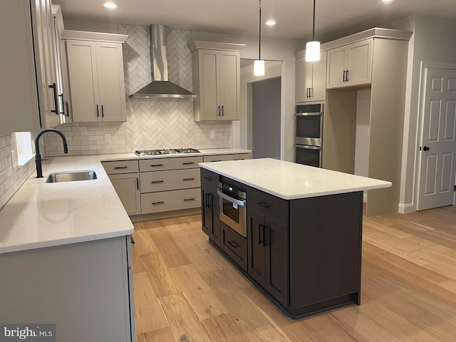 kitchen featuring sink, wall chimney range hood, decorative light fixtures, light hardwood / wood-style floors, and a kitchen island