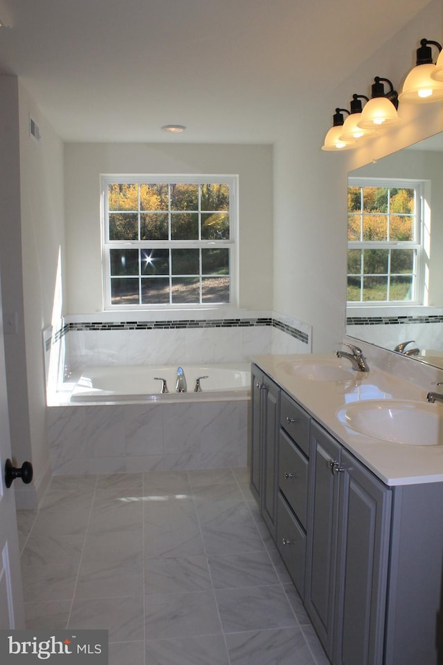 bathroom with vanity, a relaxing tiled tub, and a healthy amount of sunlight