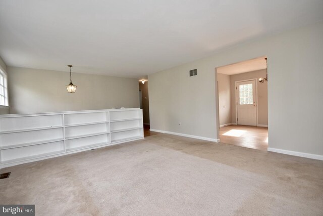 empty room with light colored carpet and an inviting chandelier