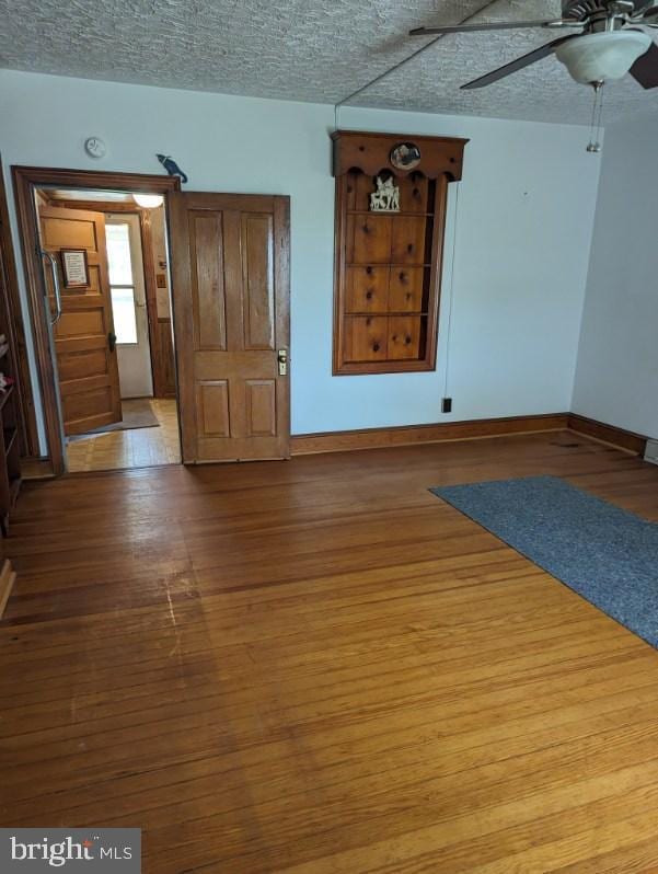 empty room with ceiling fan, wood-type flooring, and a textured ceiling