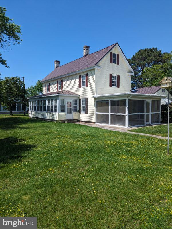 back of property with a sunroom, a yard, a chimney, and metal roof