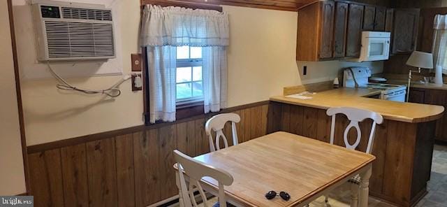 kitchen with kitchen peninsula, white appliances, a wall unit AC, and wooden walls