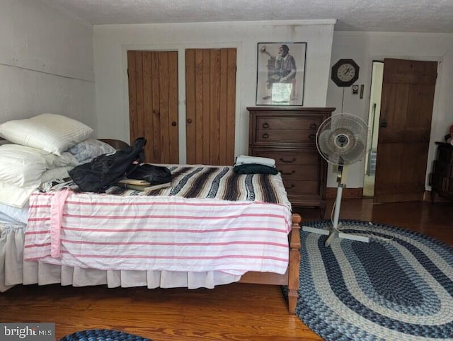 bedroom with a textured ceiling, dark wood-type flooring, and two closets