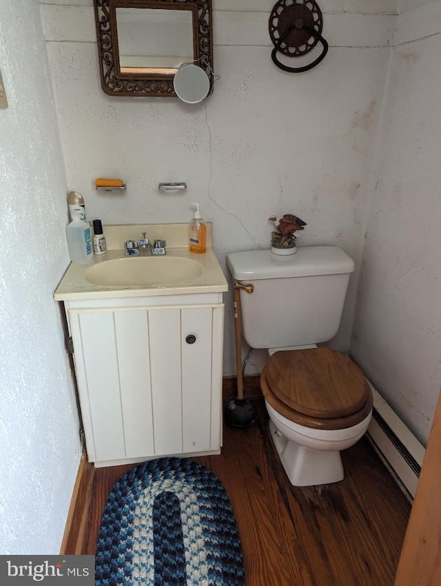 bathroom with wood-type flooring, vanity, toilet, and a baseboard heating unit