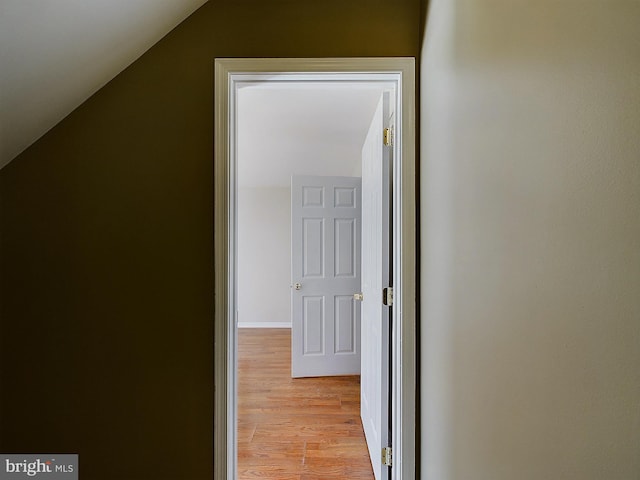 corridor with light hardwood / wood-style floors and vaulted ceiling