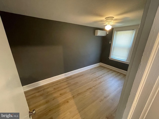 unfurnished room with a wall unit AC, ceiling fan, and light wood-type flooring