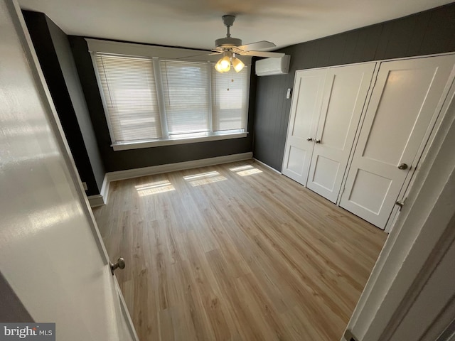 unfurnished bedroom featuring a closet, ceiling fan, light hardwood / wood-style flooring, and a wall mounted air conditioner