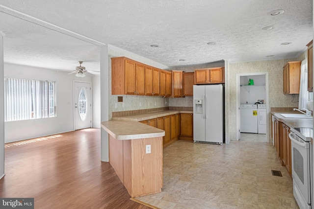 kitchen with white fridge with ice dispenser, sink, separate washer and dryer, kitchen peninsula, and range