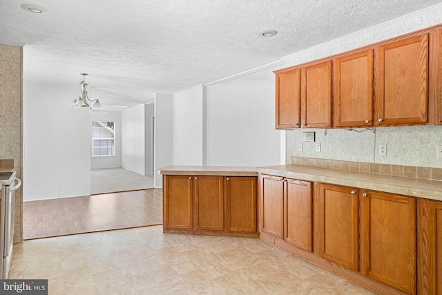 kitchen with kitchen peninsula, stove, light wood-type flooring, a textured ceiling, and an inviting chandelier