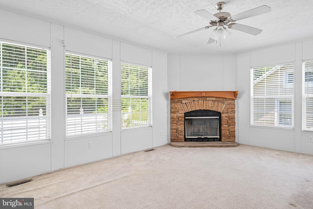 unfurnished living room with a stone fireplace, ceiling fan, carpet floors, and a textured ceiling