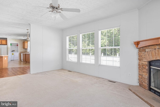 unfurnished living room with light carpet, a textured ceiling, ceiling fan, washer and dryer, and a fireplace