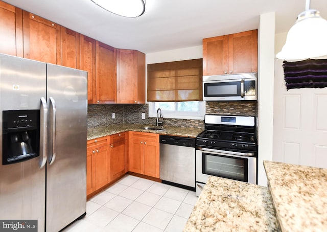 kitchen featuring sink, hanging light fixtures, appliances with stainless steel finishes, light stone countertops, and decorative backsplash