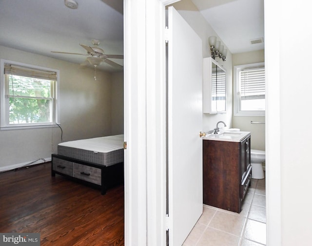 bedroom with light tile patterned flooring, ceiling fan, connected bathroom, and multiple windows