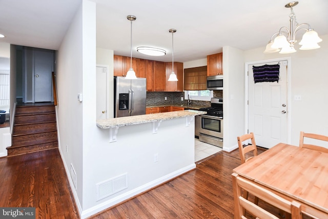 kitchen with sink, hardwood / wood-style floors, backsplash, stainless steel appliances, and kitchen peninsula