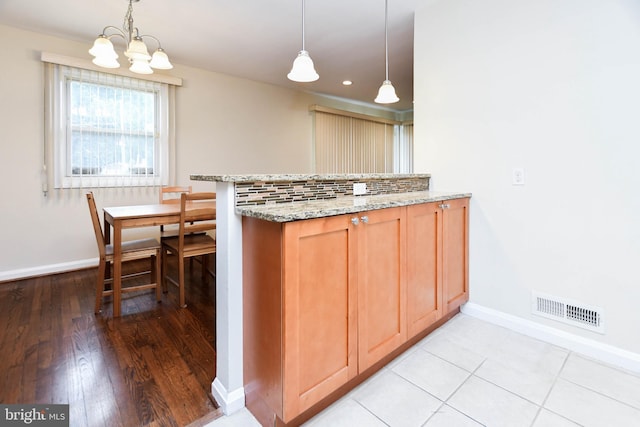 kitchen featuring hanging light fixtures, light stone countertops, and kitchen peninsula