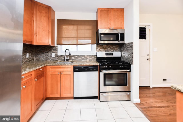 kitchen featuring light tile patterned flooring, sink, light stone counters, appliances with stainless steel finishes, and decorative backsplash