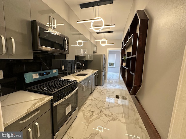 kitchen featuring decorative backsplash, appliances with stainless steel finishes, light stone countertops, sink, and decorative light fixtures