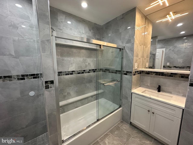 bathroom featuring vanity, bath / shower combo with glass door, and tile walls