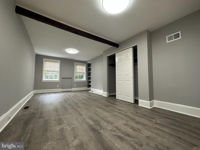 unfurnished bedroom featuring beam ceiling, dark hardwood / wood-style flooring, and a closet