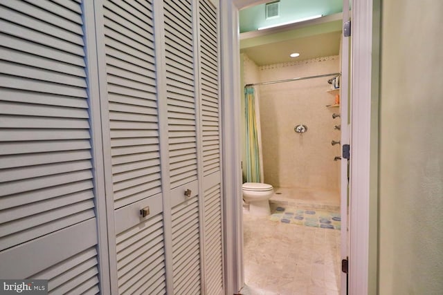 bathroom featuring tile patterned flooring, a tile shower, and toilet