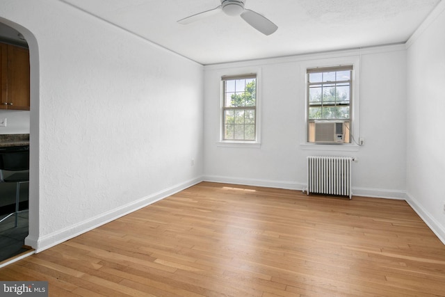 spare room featuring ceiling fan, radiator heating unit, light hardwood / wood-style floors, and ornamental molding