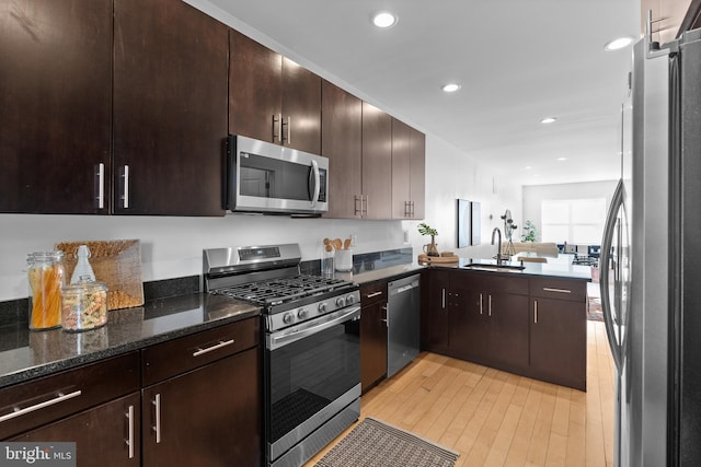 kitchen featuring appliances with stainless steel finishes, light wood-type flooring, dark brown cabinets, sink, and dark stone countertops