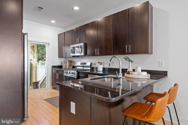 kitchen with sink, stainless steel appliances, light hardwood / wood-style flooring, dark stone counters, and a breakfast bar