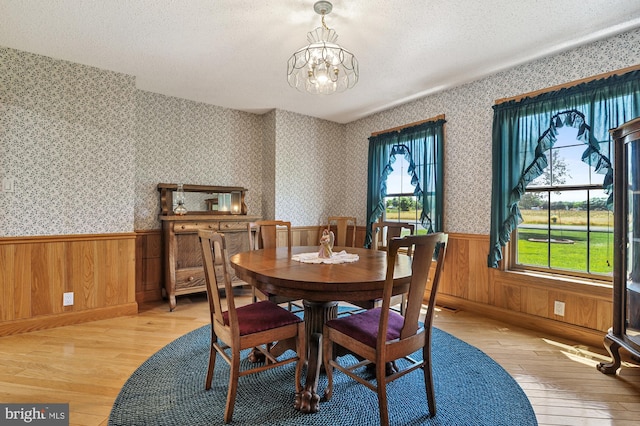 dining room featuring light wood-type flooring, a textured ceiling, wooden walls, and an inviting chandelier