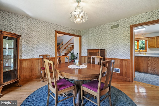 dining space with a notable chandelier, wood walls, and light hardwood / wood-style flooring