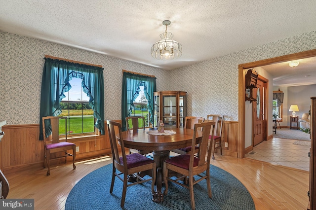 dining space with wooden walls, light hardwood / wood-style floors, and a textured ceiling