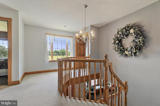 corridor with a textured ceiling, carpet floors, and an inviting chandelier