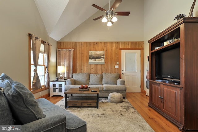 living room with wooden walls, ceiling fan, light hardwood / wood-style floors, and high vaulted ceiling