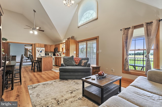 living room featuring high vaulted ceiling, light hardwood / wood-style floors, and ceiling fan with notable chandelier