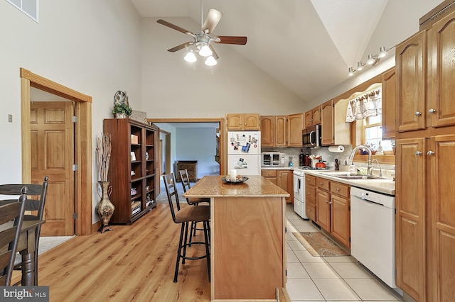 kitchen with sink, high vaulted ceiling, white appliances, a breakfast bar area, and a kitchen island