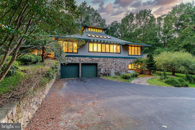 view of front facade with aphalt driveway, stone siding, an attached garage, and central air condition unit