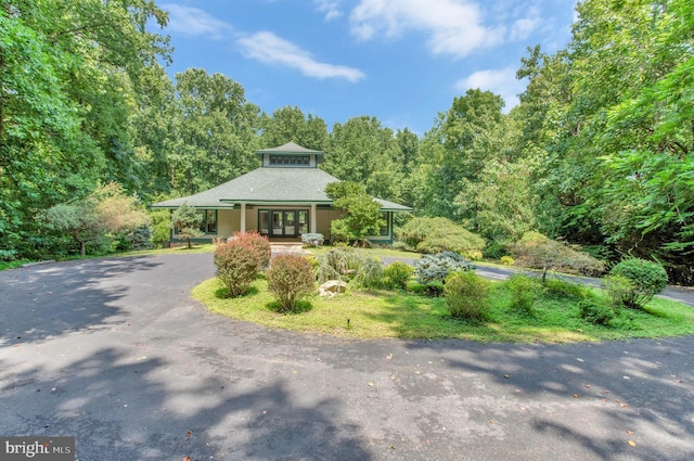 view of front facade featuring aphalt driveway, a wooded view, and french doors