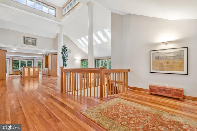 hall featuring a skylight, high vaulted ceiling, baseboards, and wood finished floors