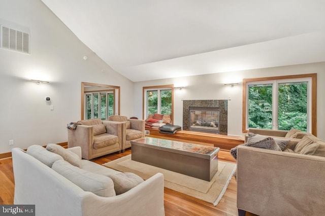 living area featuring a premium fireplace, visible vents, high vaulted ceiling, and wood finished floors