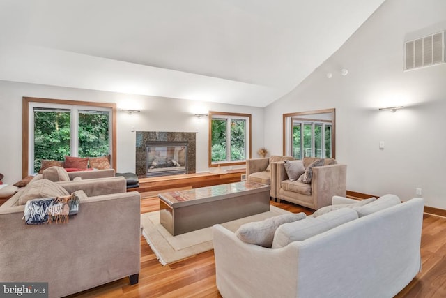 living area featuring visible vents, high vaulted ceiling, light wood-style floors, a fireplace, and baseboards