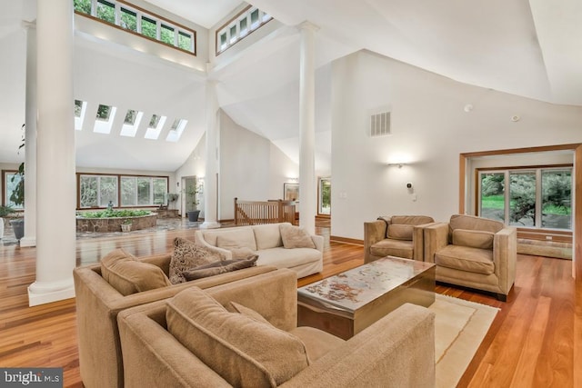 living area featuring visible vents, high vaulted ceiling, light wood-style floors, and decorative columns