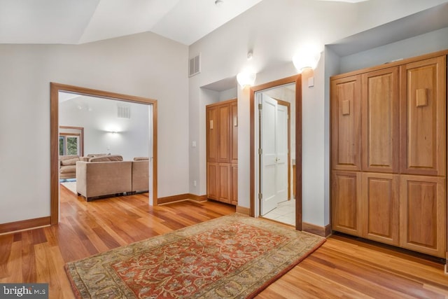 hallway featuring light wood-type flooring, visible vents, lofted ceiling, and baseboards