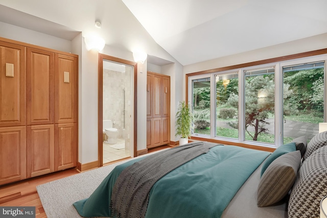 bedroom with lofted ceiling, light wood-style flooring, and connected bathroom