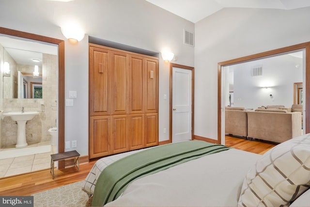 bedroom with visible vents, connected bathroom, lofted ceiling, and wood finished floors