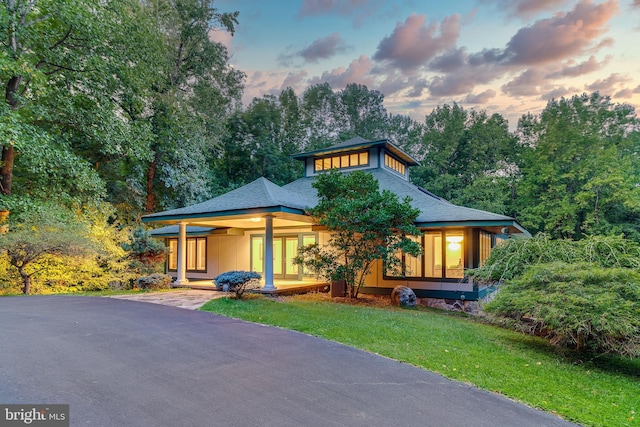 back of property at dusk with a yard, driveway, and roof with shingles