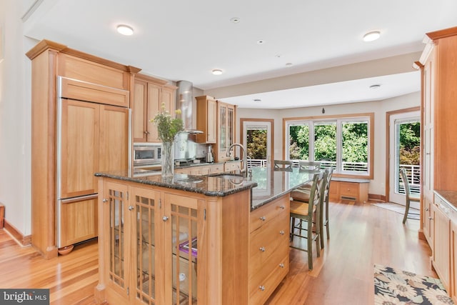 kitchen featuring a sink, a kitchen breakfast bar, wall chimney range hood, glass insert cabinets, and built in appliances